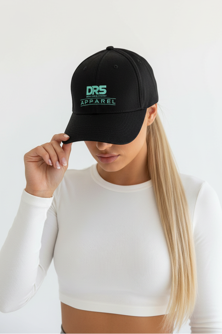 A woman wearing a black baseball cap with a green embroidered logo that reads 'DRS APPAREL', paired with a white long-sleeve crop top against a plain white background.
