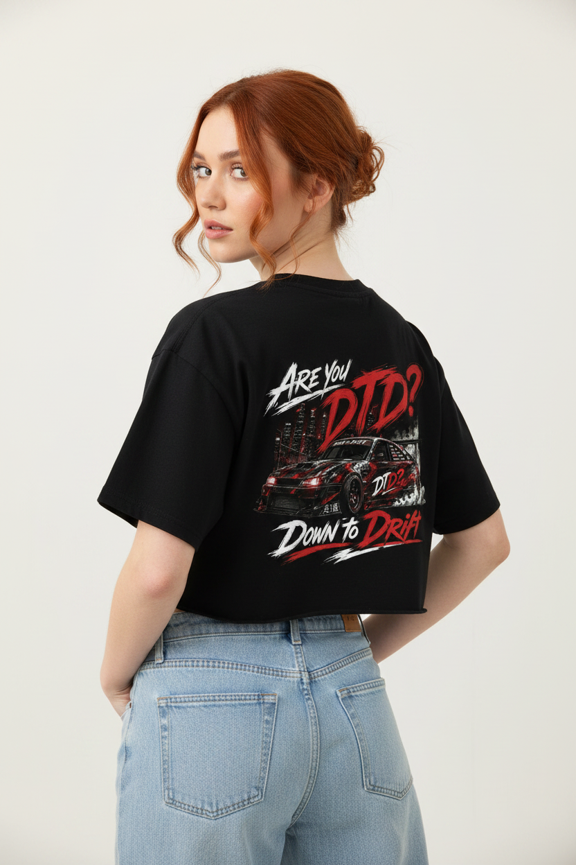 A woman with red hair is shown from the back wearing a black cropped t-shirt with a red and white 'Down to Drift' graphic print, paired with light blue jeans, against a plain light gray background.
