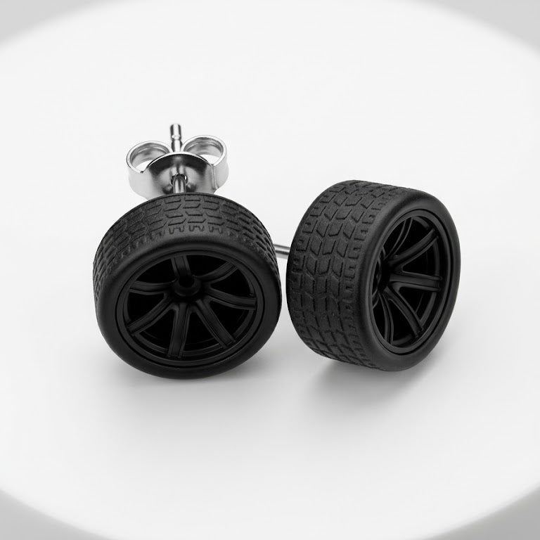 A pair of black stud earrings designed to look like miniature car wheels with textured treads and multi-spoke rims, shown on a white circular pedestal.