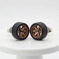 A pair of miniature toy wheels with black textured tires and bronze-colored multi-spoke rims, displayed on a white ceramic pedestal against a white background.
