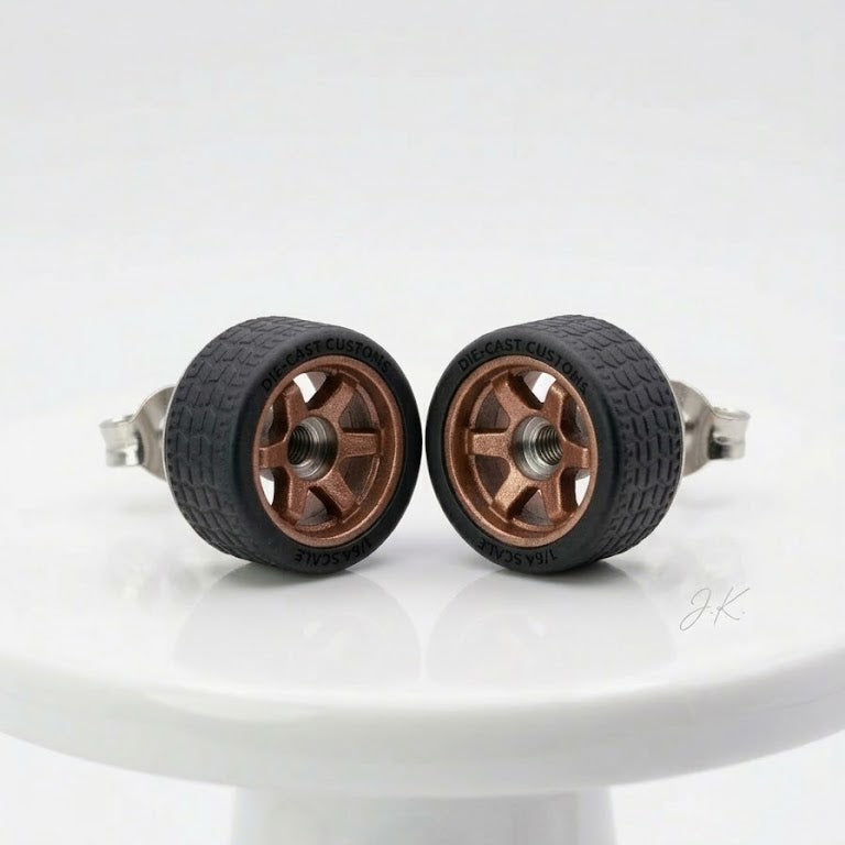 A pair of miniature toy wheels with black textured tires and bronze-colored multi-spoke rims, displayed on a white ceramic pedestal against a white background.