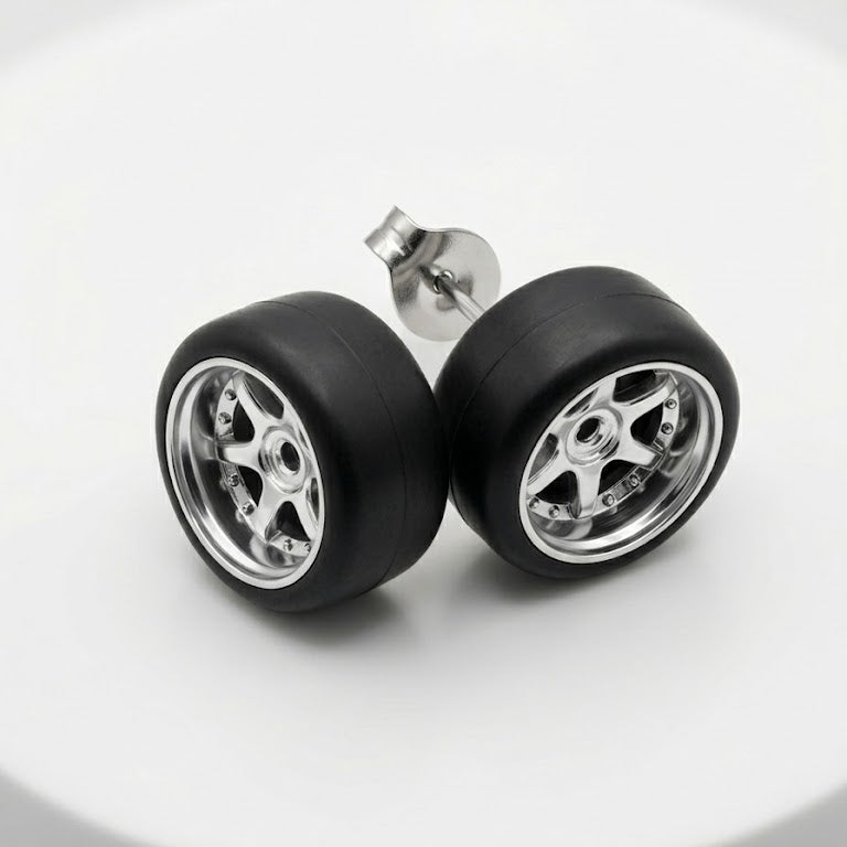 A pair of stud earrings designed to look like miniature car wheels, featuring black tires and silver multi-spoke rims, displayed on a clean white surface.