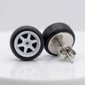 A pair of stud earrings designed to look like miniature toy car wheels, featuring black tires and white multi-spoke rims, with one earring turned to show the silver butterfly back.